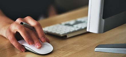 Hand on a computer mouse behind a computer screen