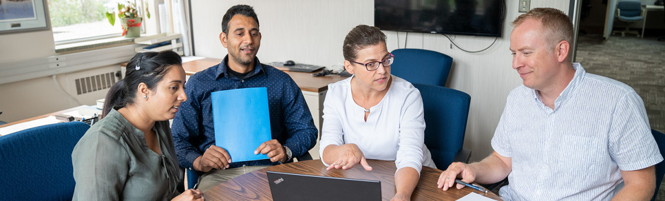 Employees sitting around meeting table with computer