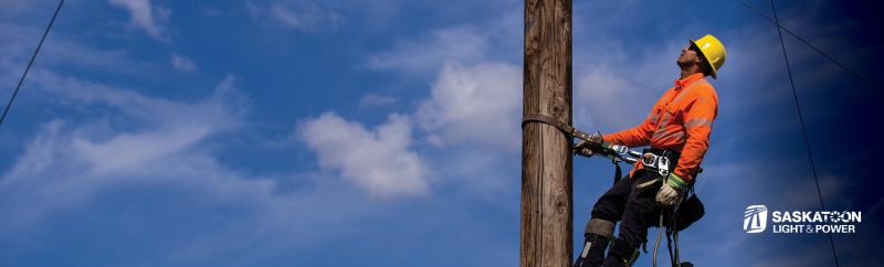 A lineworker in high viz and a safety harness climbs a power pole